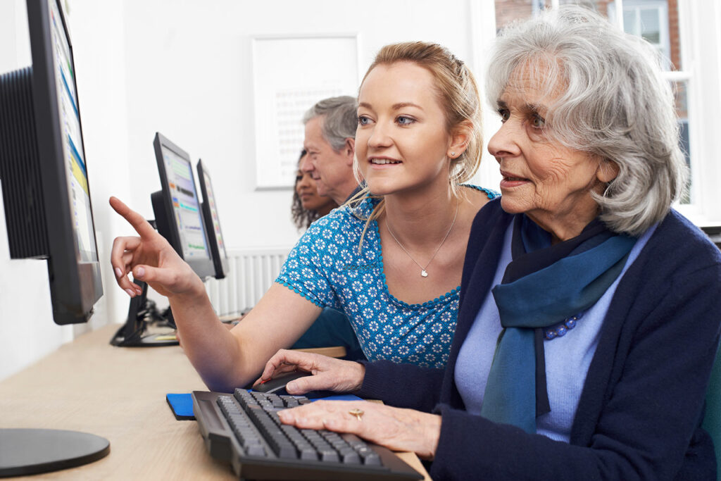 Frau erklärt am Computer einer Seniorin etwas