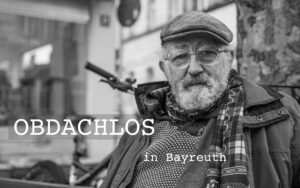 Filmtitel "Obdachlos in Bayreuth" und Foto von Roland, älterer Mann mit Brille, Bart, Baskenmütze