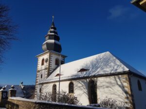 Vor einem strahlend blauen Himmel steht die Kirche mit Zwiebelturm auf der linken Seite.