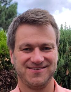 Mann mit Bart vor einer grünen Hecke im Portrait