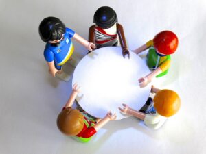 Fünf Figuren sitzen, angeschaut von oben, um einen weißen Tisch