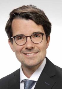 Man sieht das Gesicht eines braunhaarigen Mannes mit Brille.