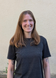 Junge Frau mit langen, glatten Haaren vor einer hellen Hauswand.