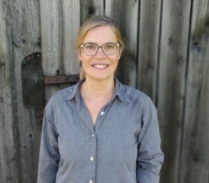 Kursleiterin Antje Ricken  in blauem Hemd vor Holzwand.