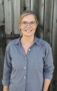 Referentin Antje Ricken in blauem Hemd vor Holzwand.