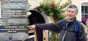 Pilgerführer Michael Thein zeigt mit ausgestrecktem Arm auf einen Wegweiser aus Holz