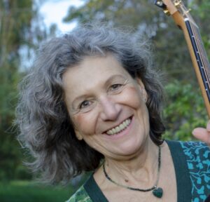 Porträtfoto der Kursleiterin: graue gewellte Haare, Gitarre in der Hand.