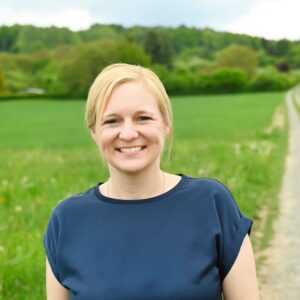 Referentin Annkathrin Döpfner-Uffmann: Junge blonde Frau mit blauem T-Shirt vor Wiese.